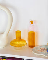 Styled image featuring the Ichendorf Milano Pink/Amber Light Colore Bottle, Amber/Clear Alchemy Decanter, and E.E. Ceramics Flower Serving Platter.