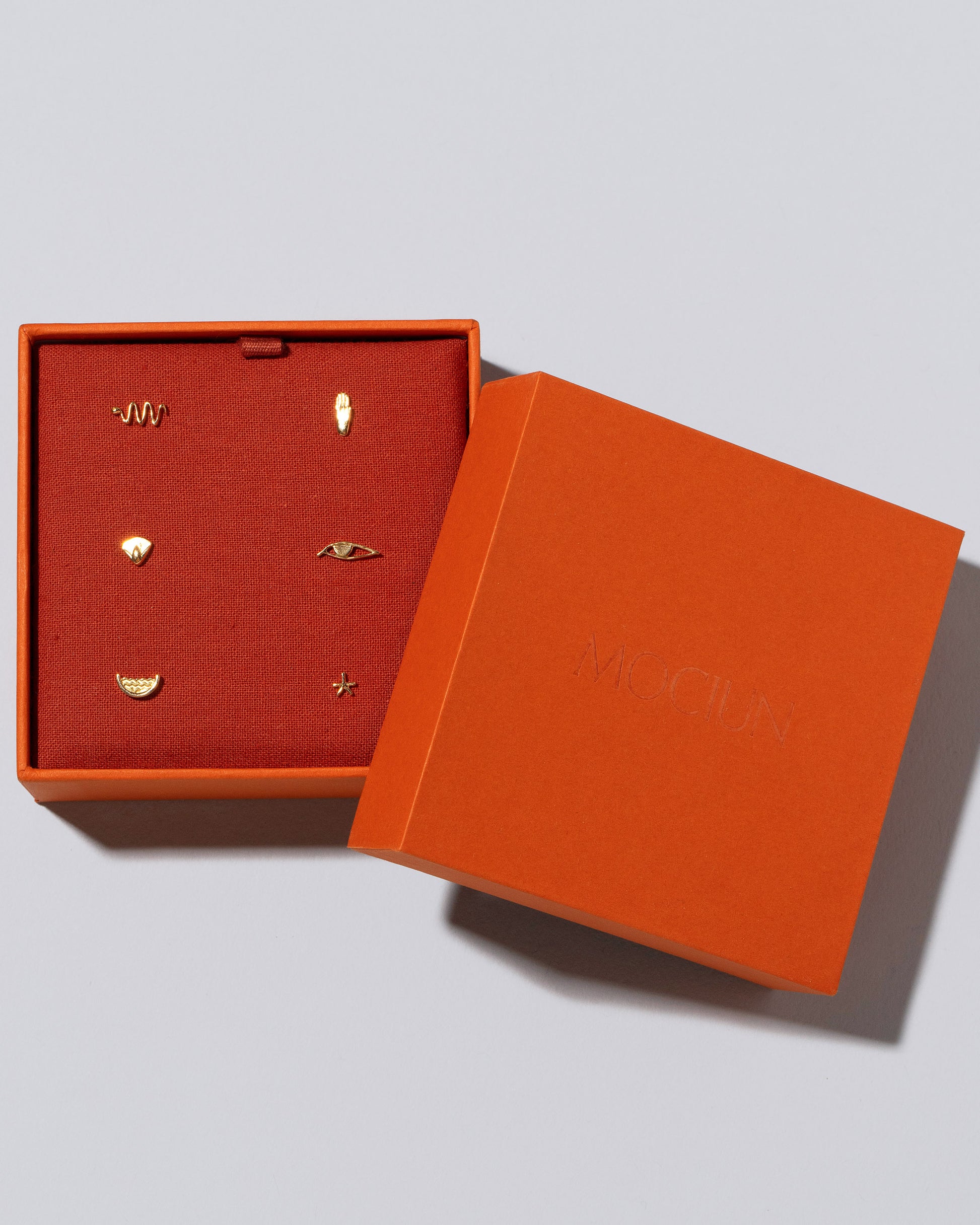Six Talisman Stud Earring Singles Set in Mociun Box on light color background.