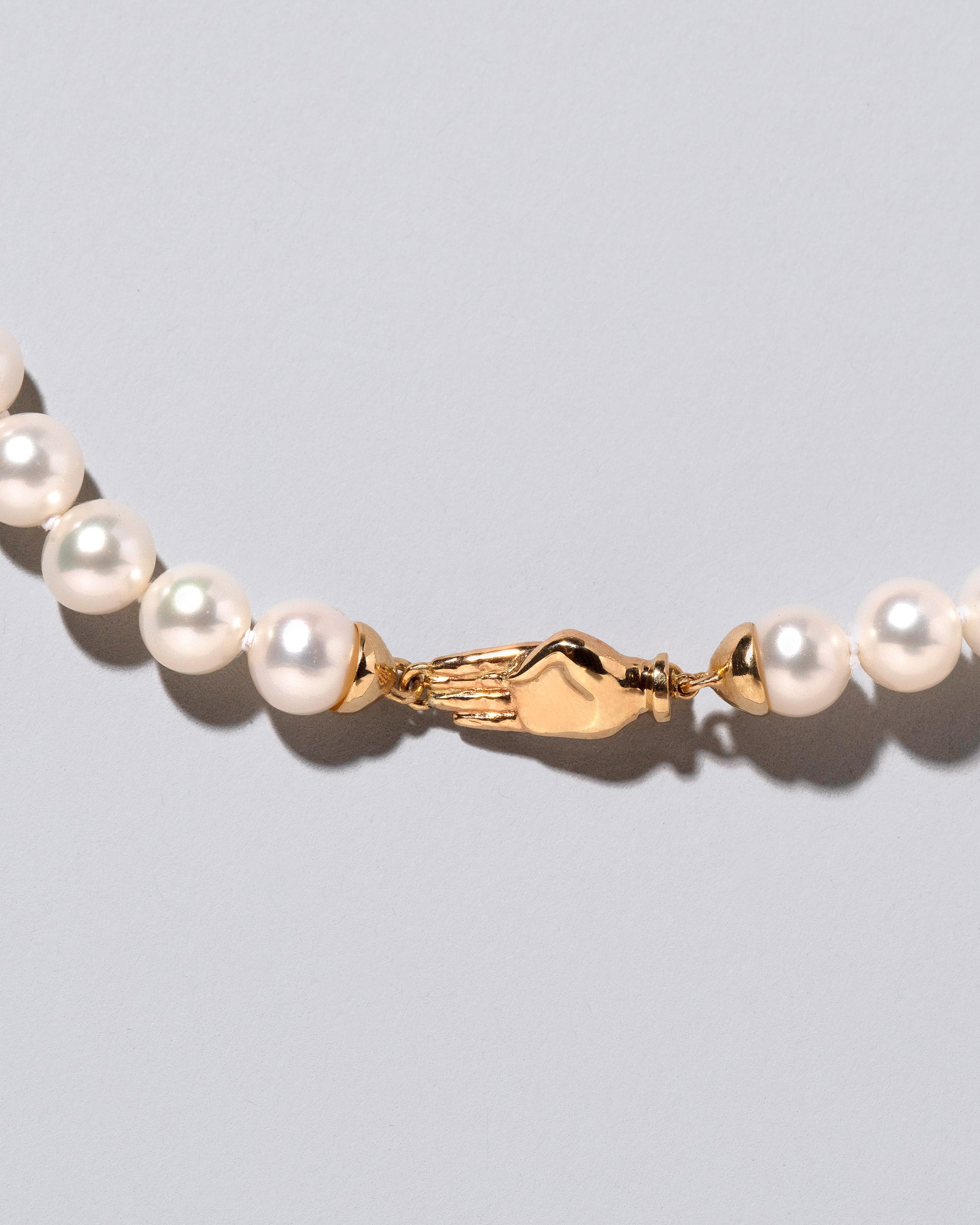 Closeup detail of the back of the White Pearl & Yellow Gold Union Pearl Necklace on light color background.