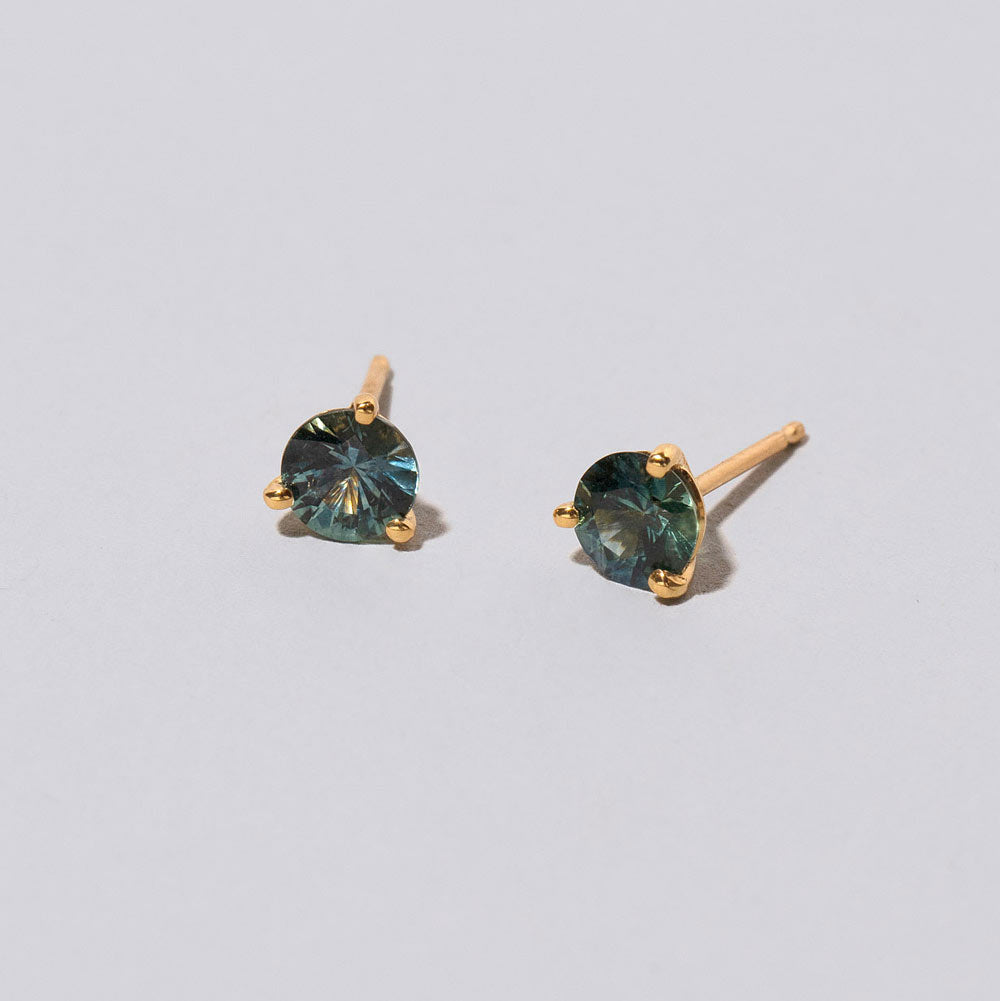 product_details::Closeup details of the Mega Blue Sapphire Martini Stud Earrings on light color background.