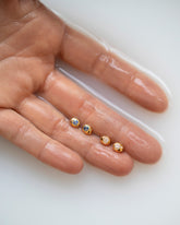 Yellow Gold Bicolor Blue Sapphire Level Stud Earrings and Yellow Gold Diamond Level Stud Earrings in hand.