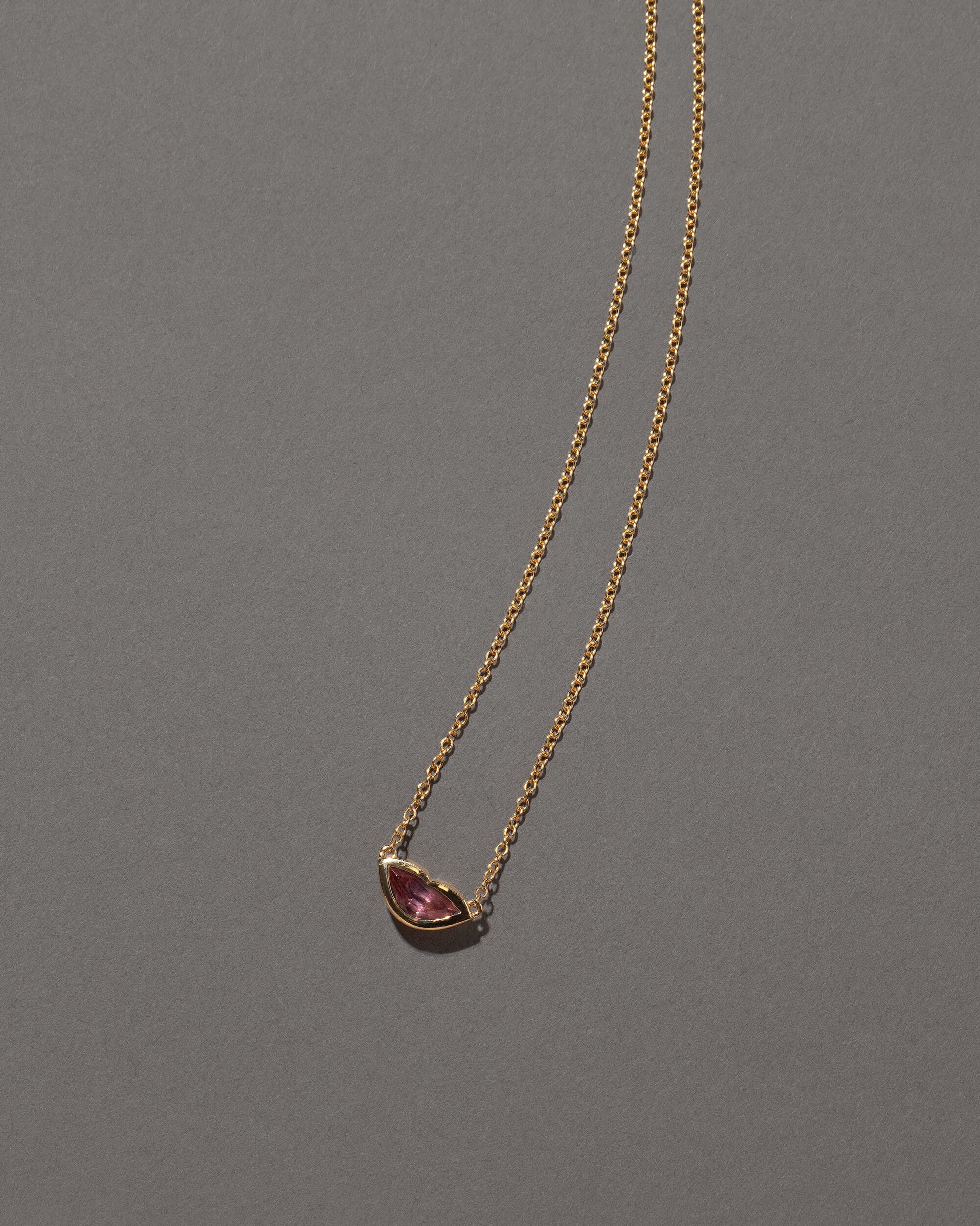Closeup details of the Peach Spinel Lover's Kiss Necklace on grey color background.