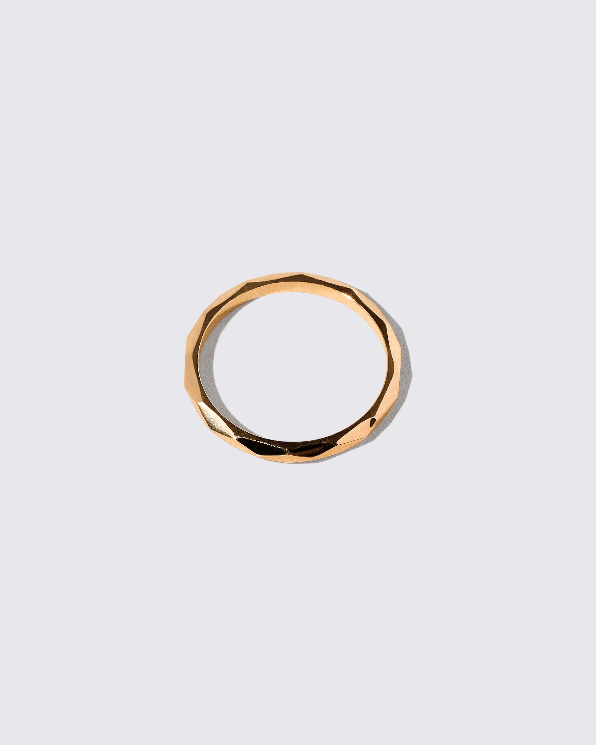 Closeup details of the Gold 2mm Facet Band on light color background.