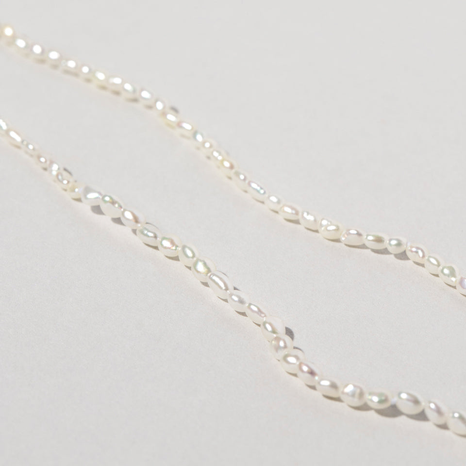 product_details::Closeup details of the White Oval Seed Pearl Bracelets on light color background.