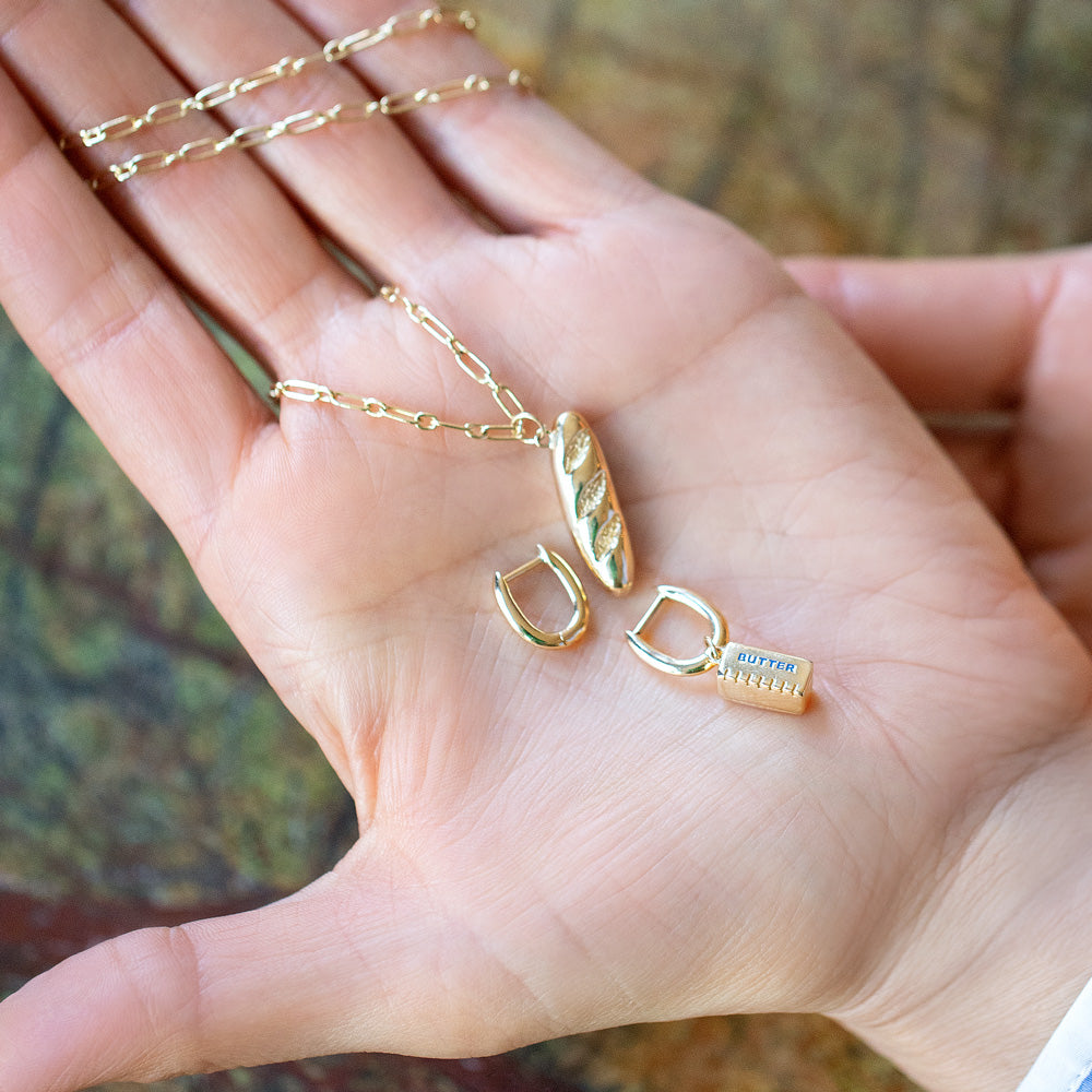 product_details::Hot Dog Chain Necklace with Demi Baguette Charm and Stick of Salted Butter Charm paired with the Huggie components of the Solid Gold Link Huggie Hoop Earrings on model.