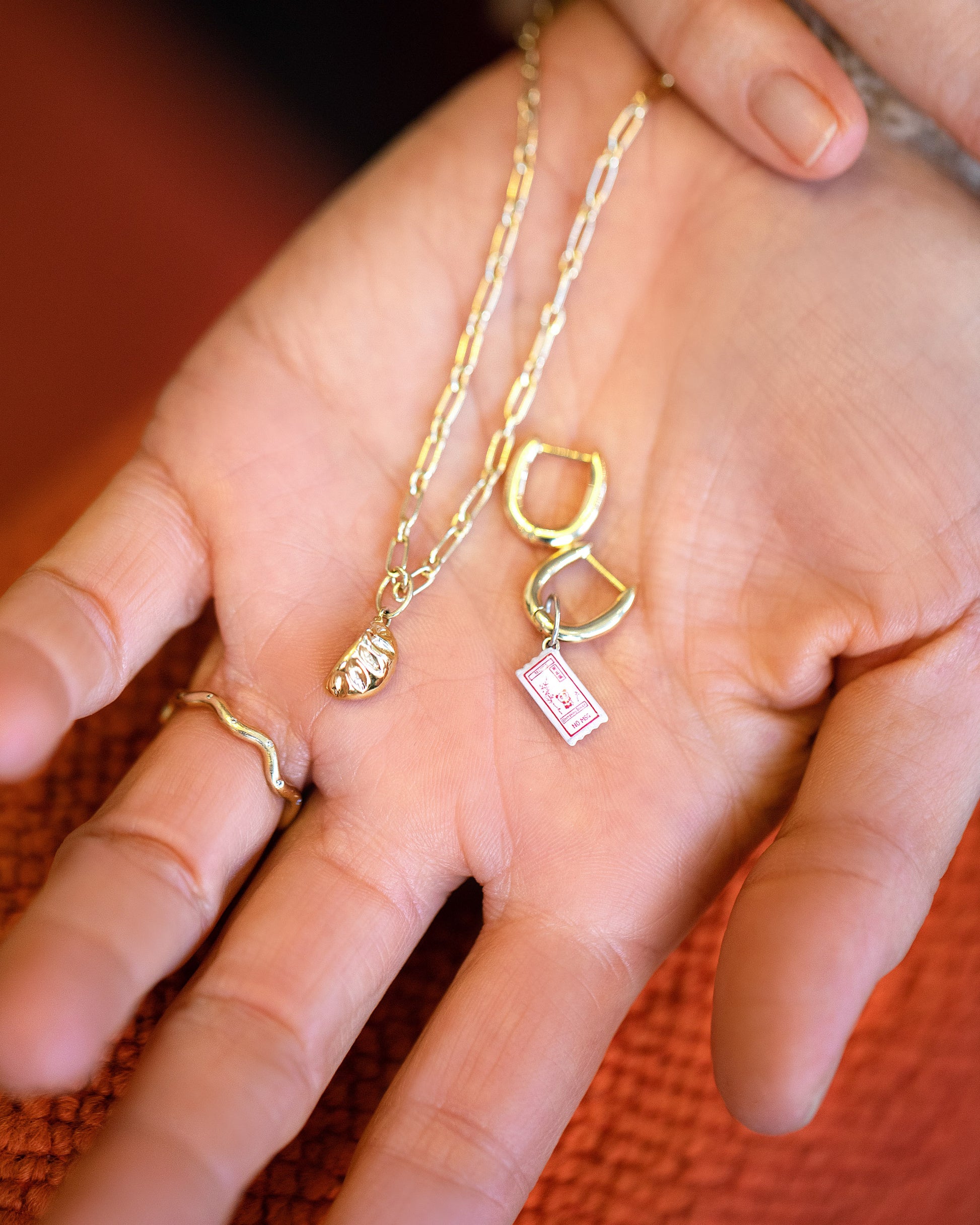 Hot Dog Chain Necklace with Steamed Dumpling Charm, Dumpling Sauce Packet Charm paired with the Huggie components of the Solid Gold Link Huggie Hoop Earrings and Gold Bump Band on model.