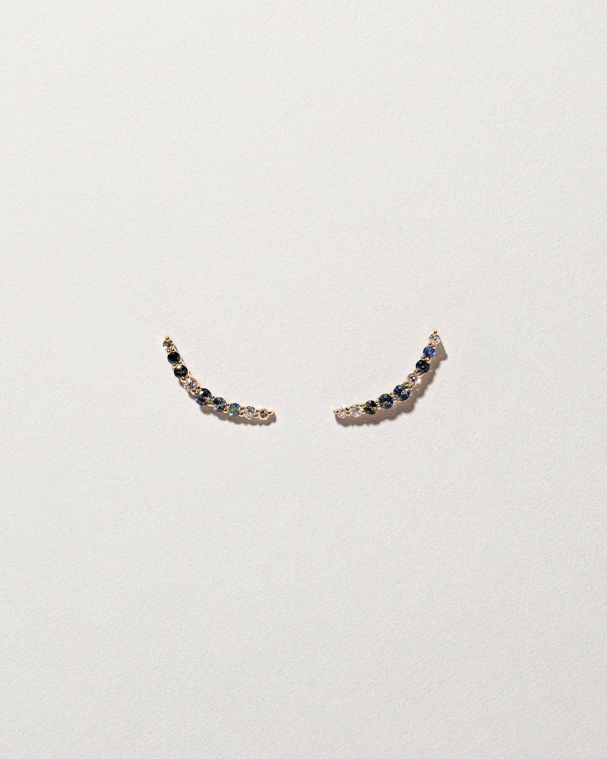 An edition of the Sapphire & White Diamond Crescent Ear Climber Stud Earrings on light colored background.