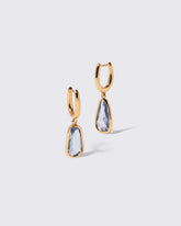 Blue Sapphire Gusher Charm Huggie Hoop Earrings on light color background.