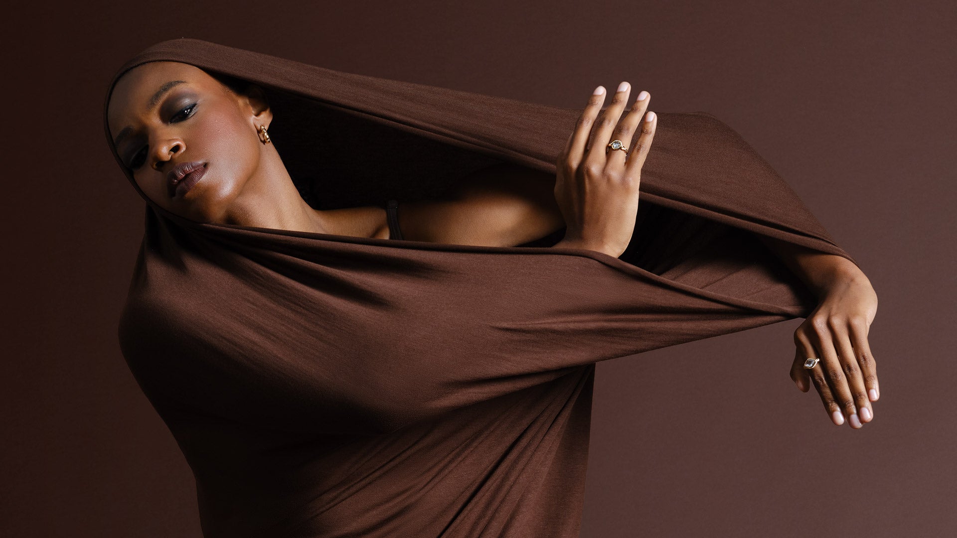 Model wrapped in a dark brown fabric against a matching background and wearing rings from the Twist Collection.