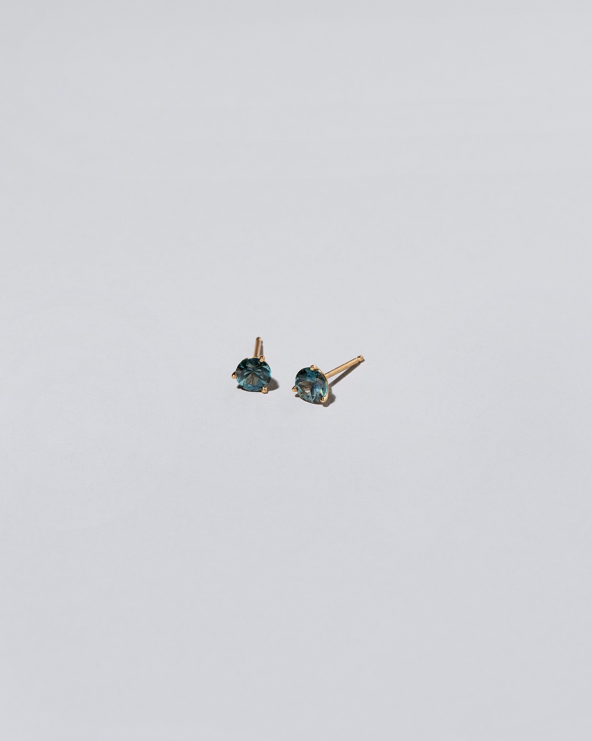 Teal Bicolor Sapphire Martini Stud Earrings on light color background.