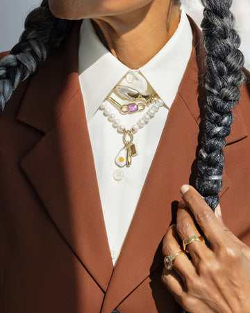 Styled image on model featuring the Gold 5mm Ripple Band, Pearl Link Huggie Hoop Earrings, the Frank Fish Brooch pinned on the collar above the Sapphire Gusher Openable Pendant on Link Necklace, and on clasp of the Gold Pearl Openable Link Necklace is a Demi Baguette Charm, Stick of Salted Butter Charm and Fried Egg Pendant.