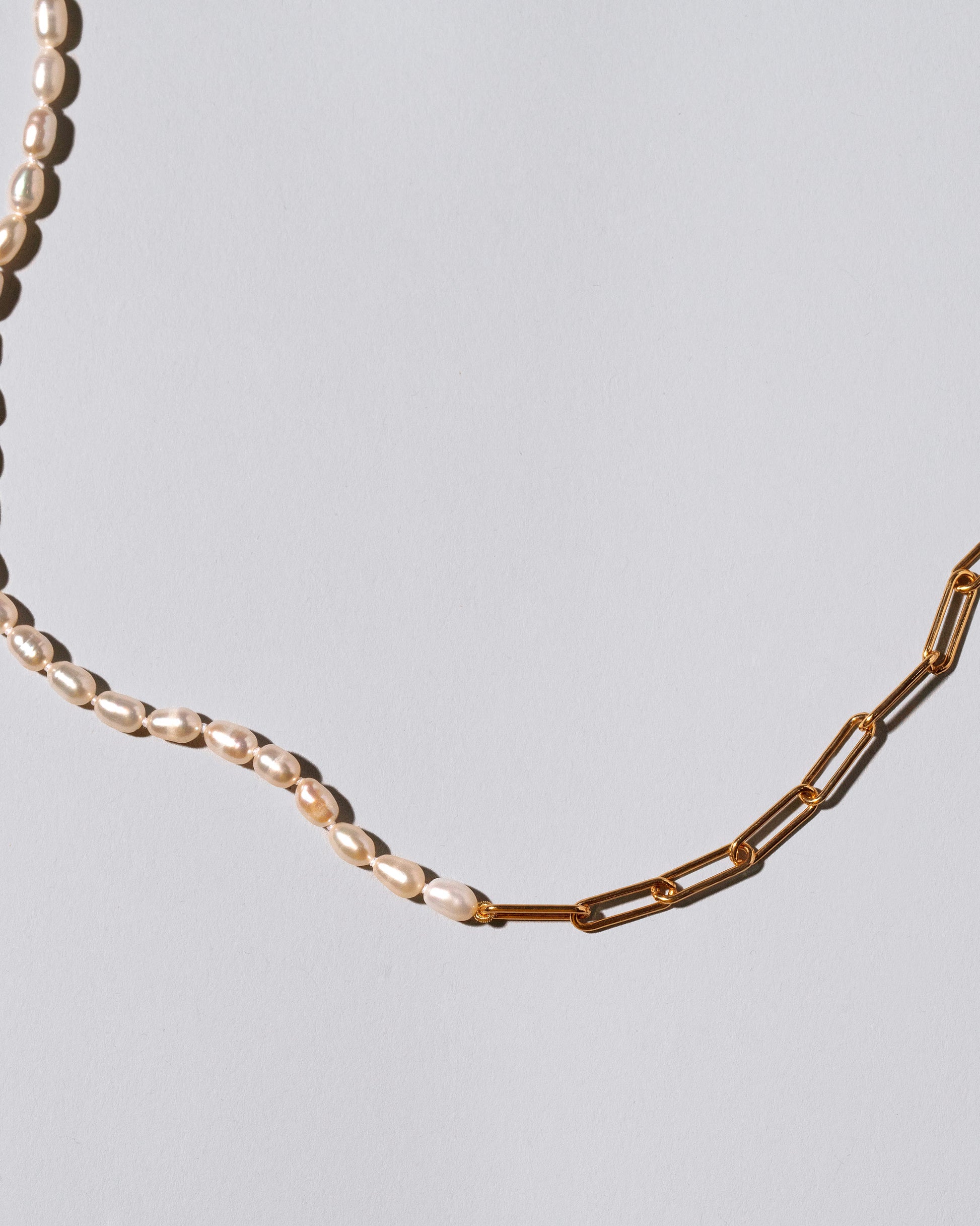 Closeup detail of the Rice Pearl Long Oval Necklace on light color background.