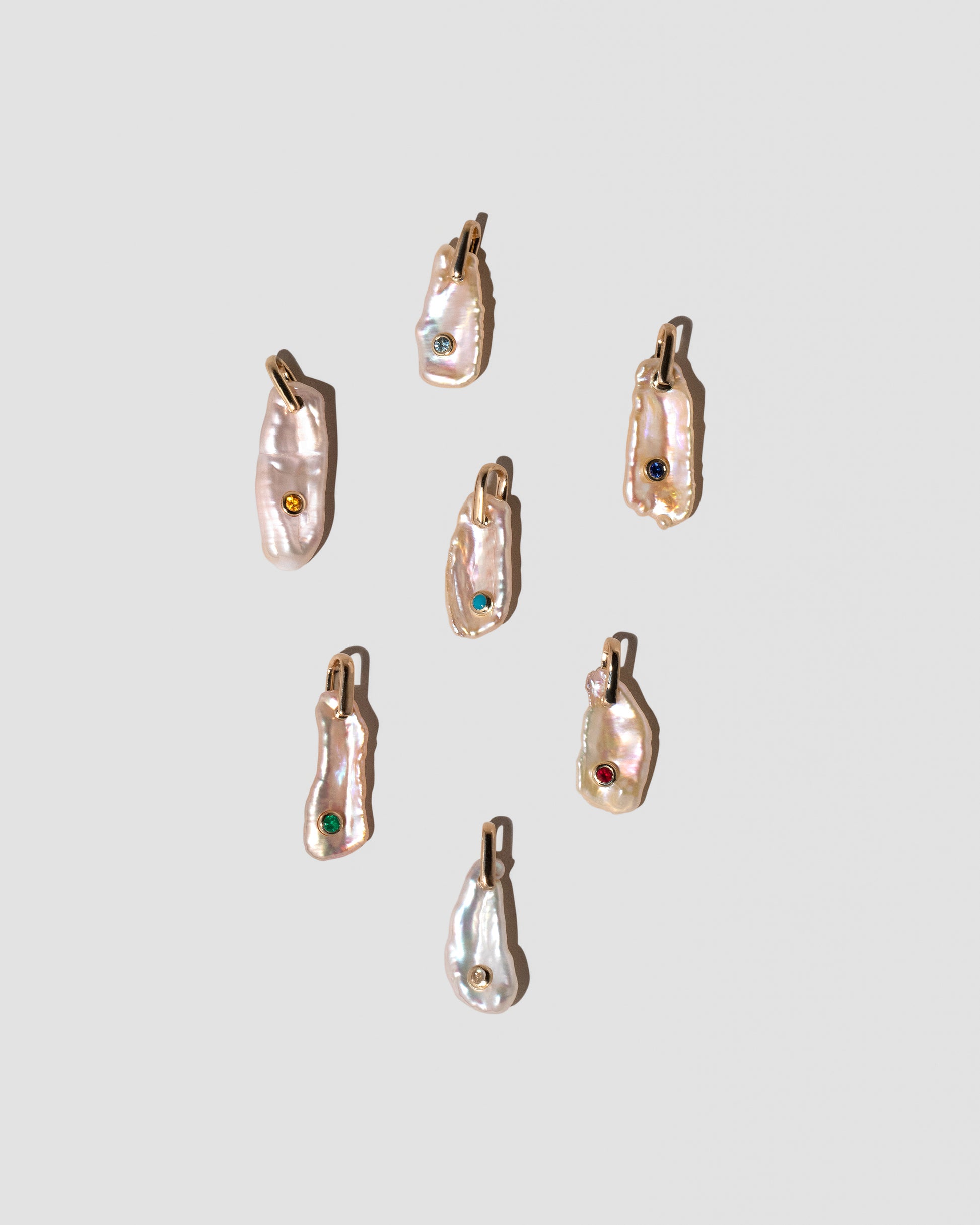 March Birthstone Pearl Pendant With Aquamarine, November Birthstone Pearl Pendant With Citrine, September Birthstone Pearl Pendant With Sapphire, December Birthstone Pearl Pendant With Turquoise, May Birthstone Pearl Pendant With Emerald, September Birthstone Pearl Pendant With Sapphire, January Birthstone Pearl Pendant With Garnet and June Birthstone Pearl Pendant With Moonstone on light color background.