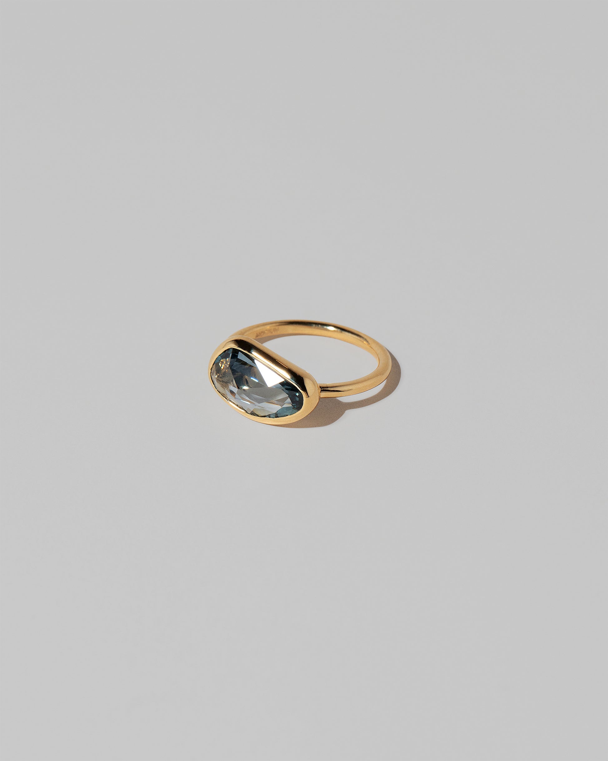 View from the side of the Gusher Teal Sapphire Ring 037 on light color background.