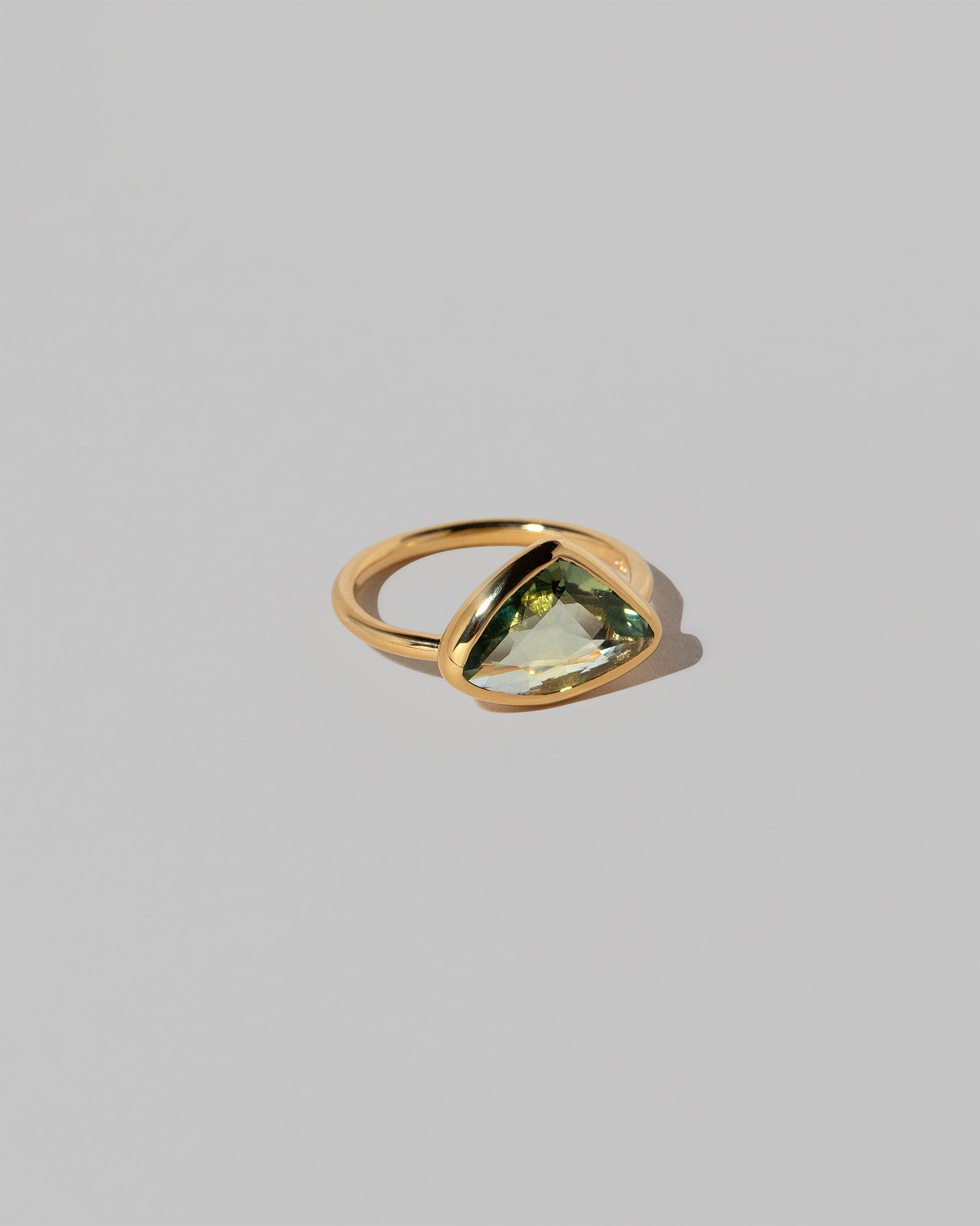 View from the side of the Gusher Green Sapphire Ring 036 on light color background.