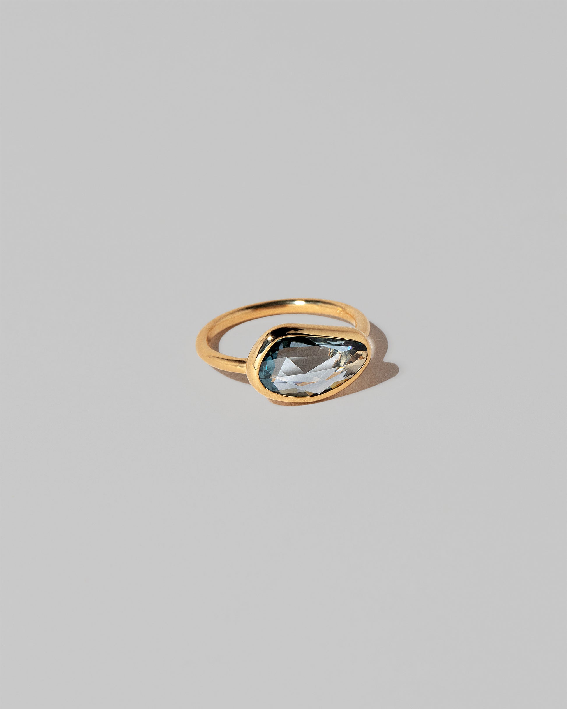 View from the side of the Gusher Teal Sapphire Ring 037 on light color background.