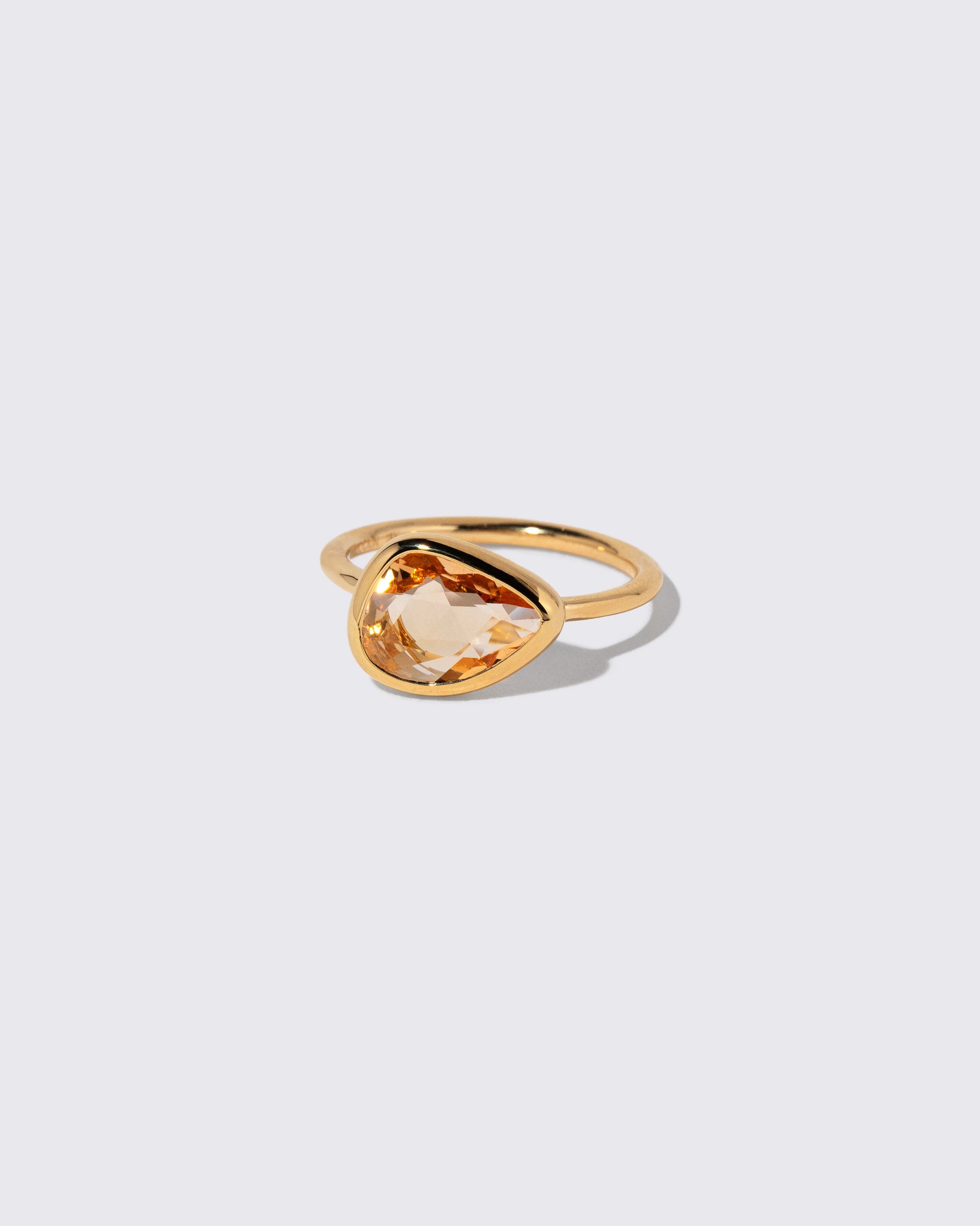 View from the side of the Peach Pink Sapphire Gusher Ring on light color background.
