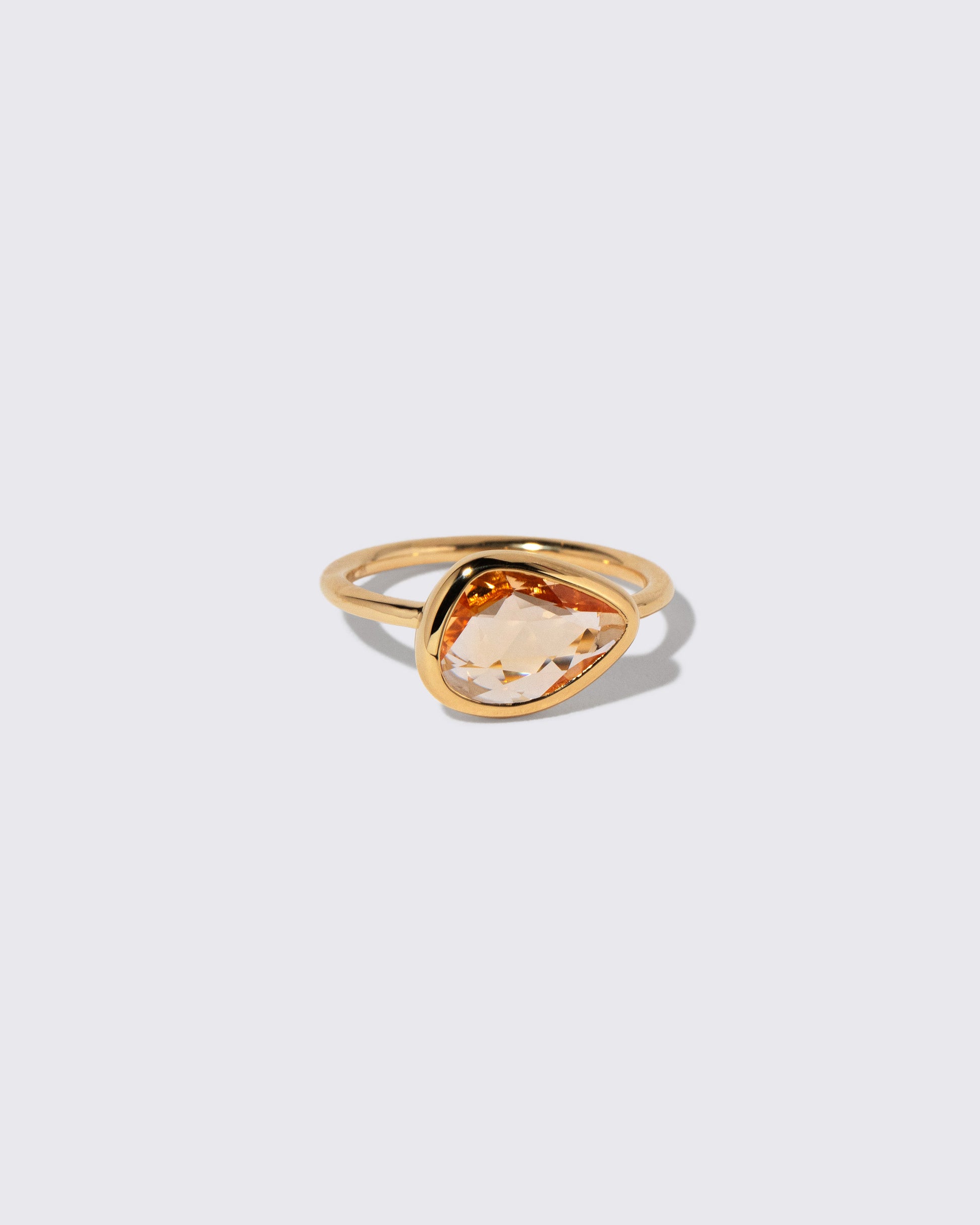 View from the side of the Peach Pink Sapphire Gusher Ring on light color background.