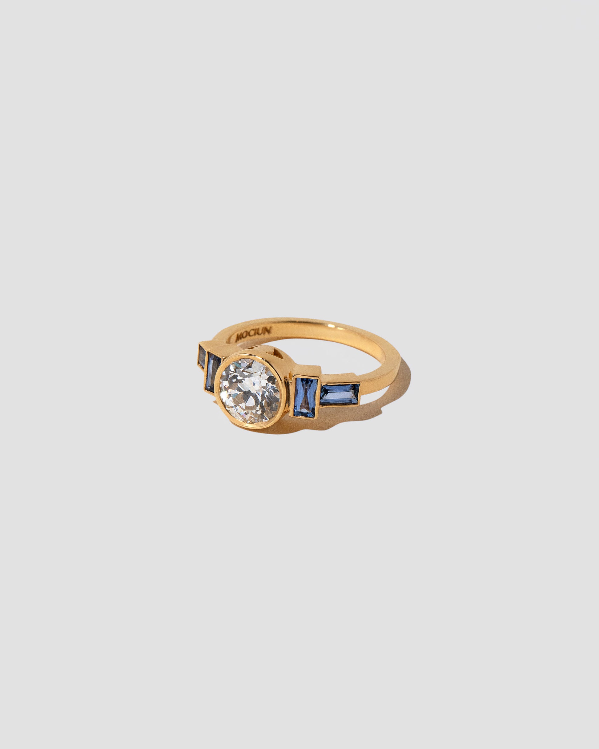 View from the side of the White Diamond & Blue Sapphire Third Eye Ring on light color background.