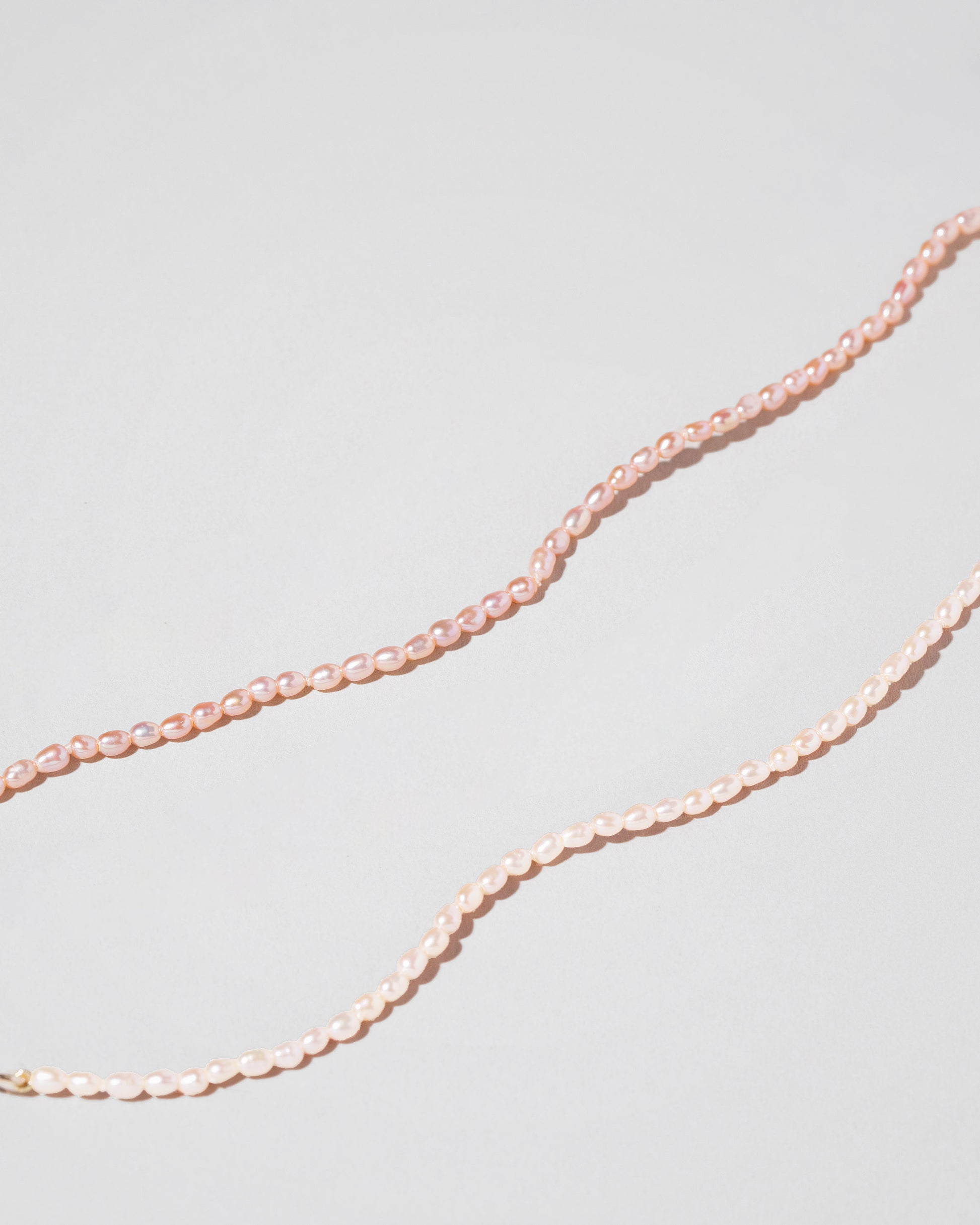 Closeup details of the Pink Peony Oval Pearl Necklace and White Oval Pearl Necklace on light color background.