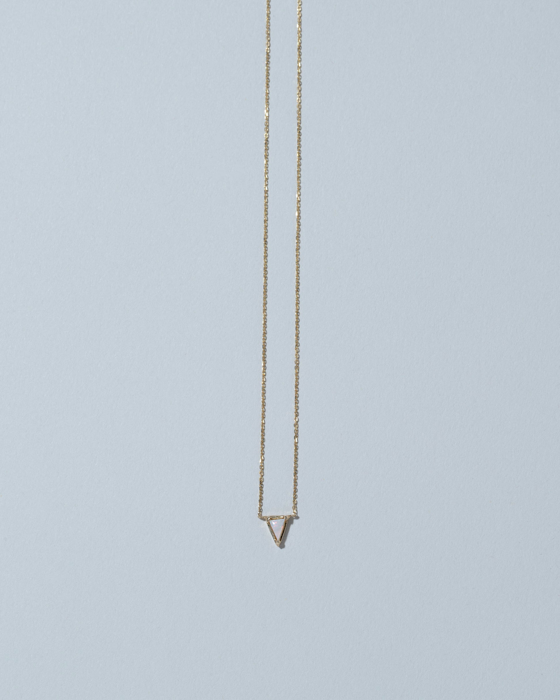 Gold White Opal Triangle Necklace on light color background.