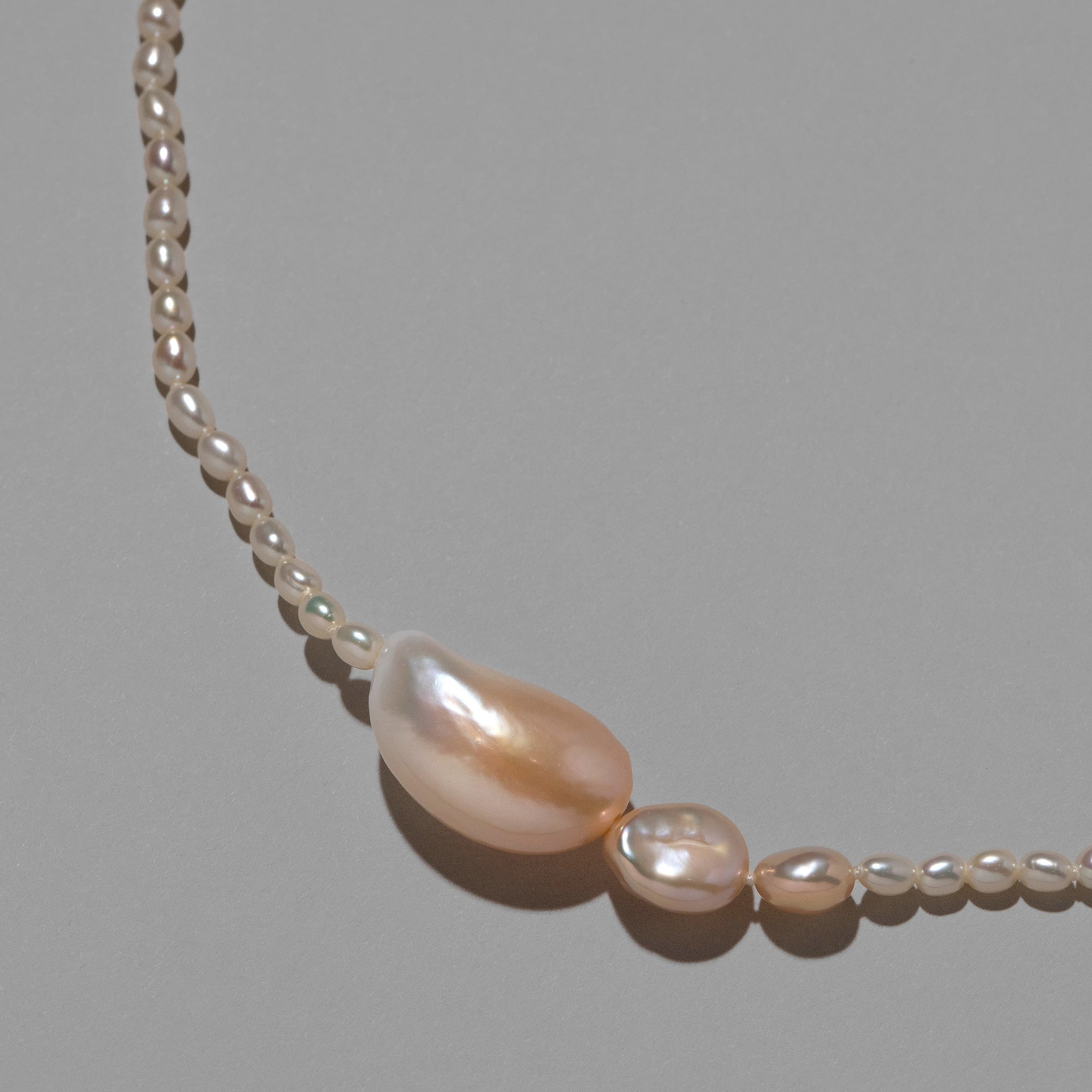 product_details::Closeup details of the Nereus Pearl Necklace on light color background.