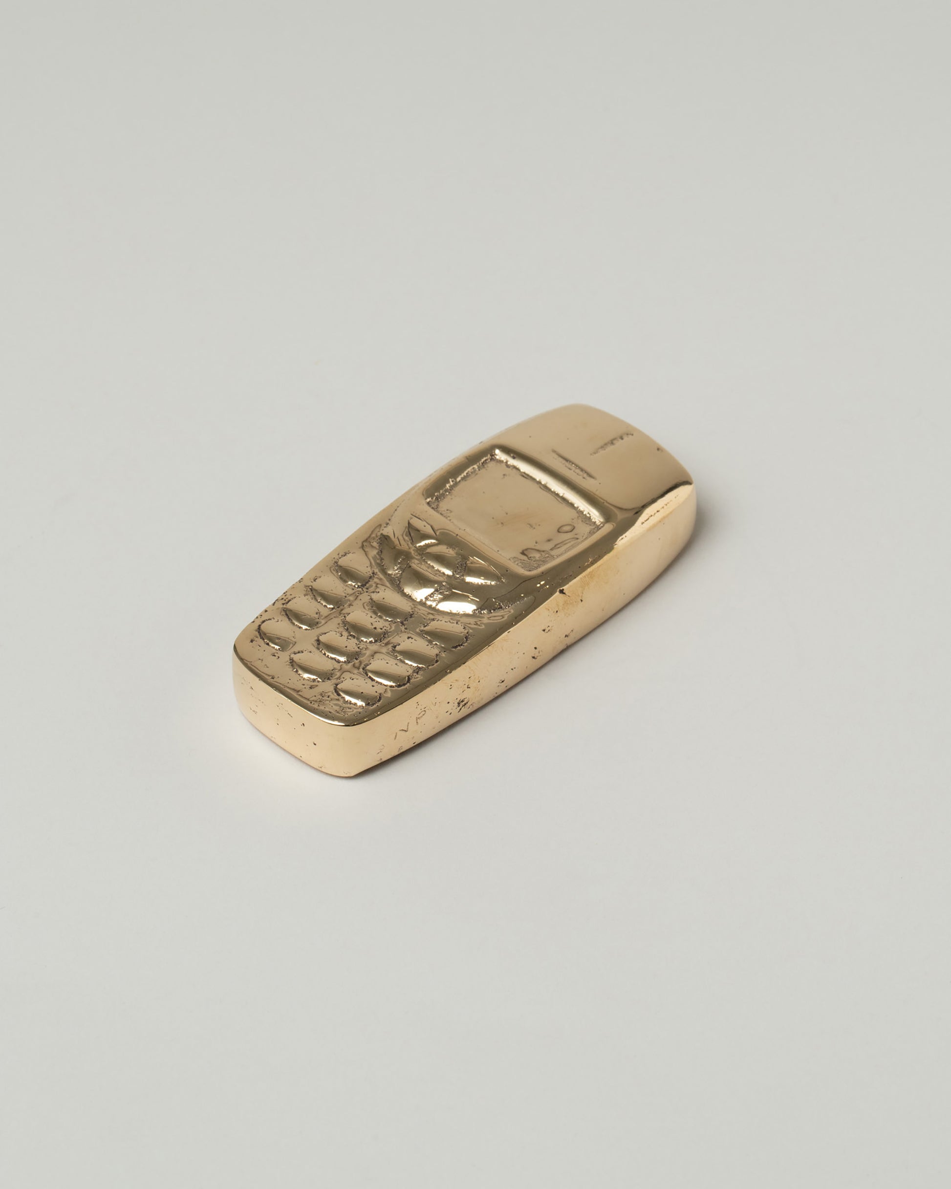 View from the side of the Pearce Objects Cast Bronze Nokia™ Brick Phone on light color background.