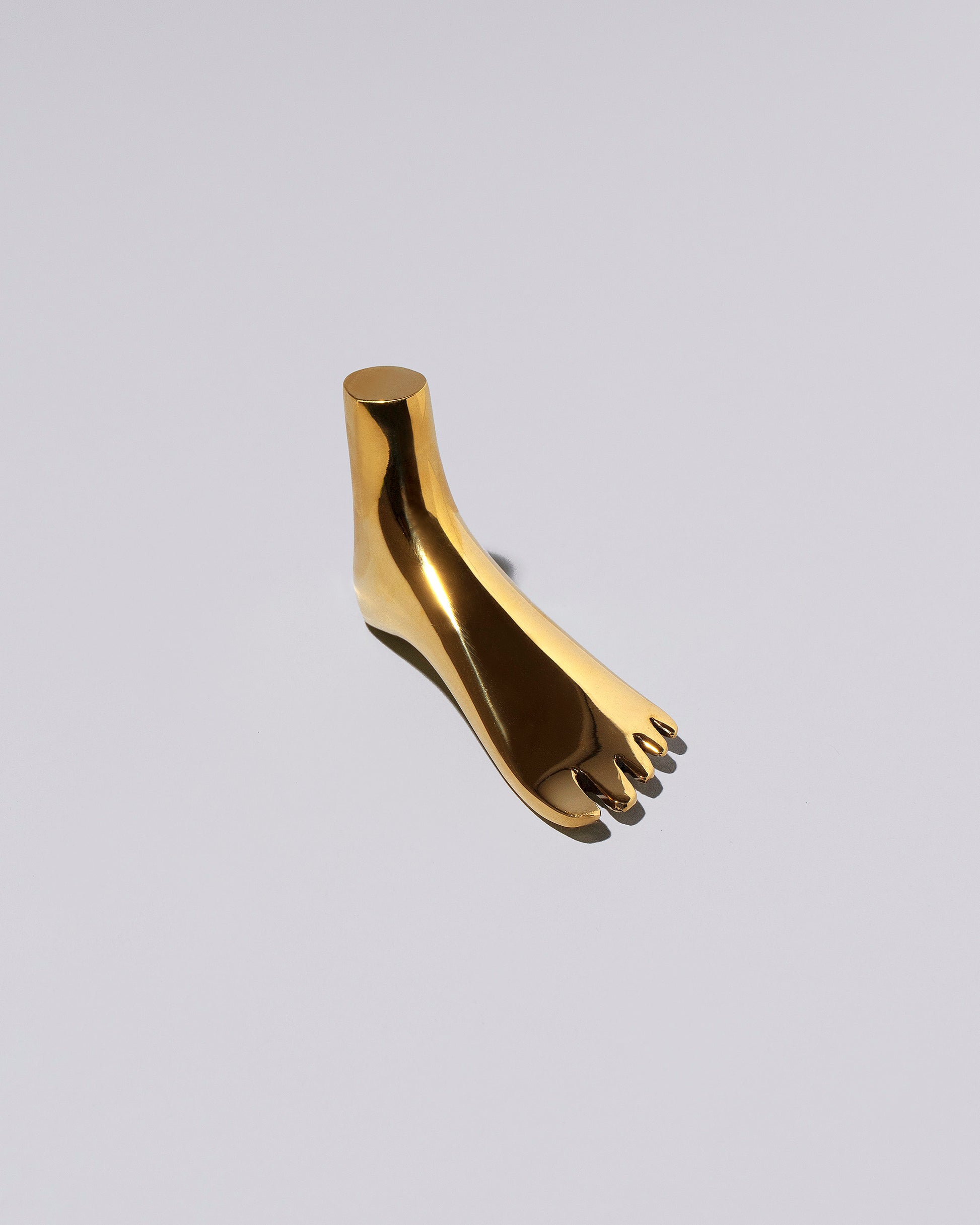View from the side of the Carl Auböck Brass Foot Paperweight on light color background.