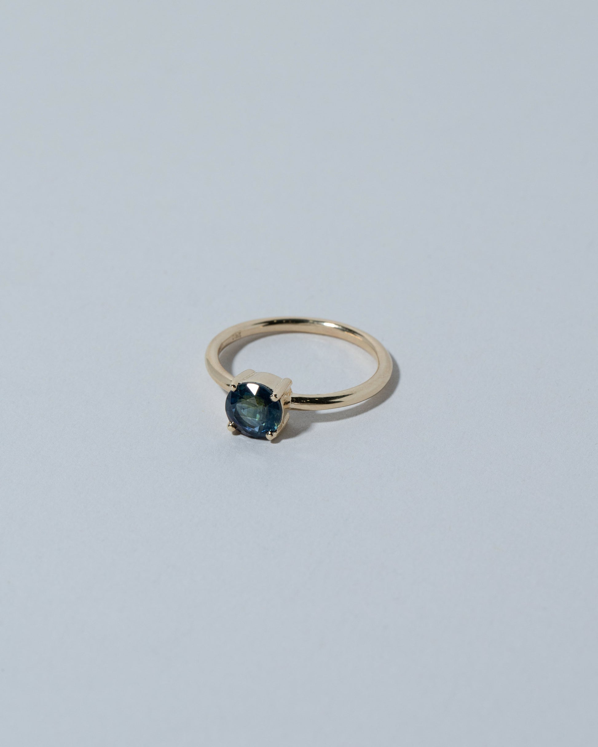 View from the side of the Samples & Imperfects 14k Yellow Gold Round Blue Sapphire Ring on light color background.