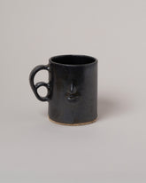 Rami Kim Face Mug With Double Loop Handle on light color background.