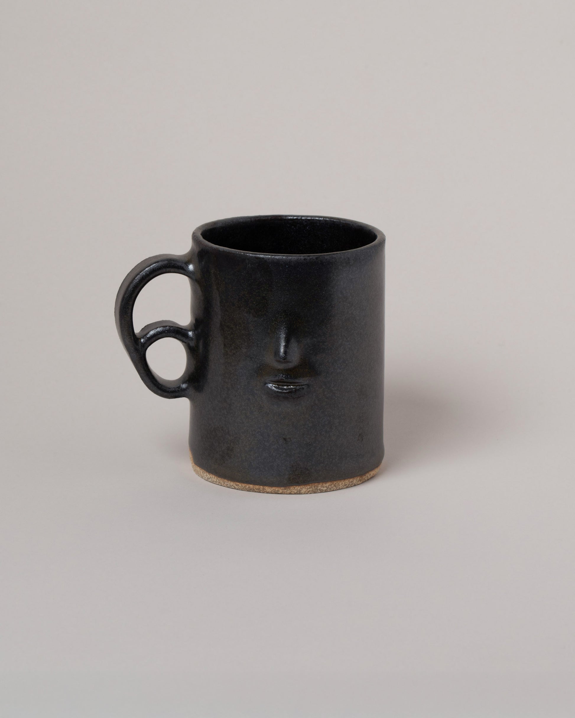 Rami Kim Face Mug With Double Loop Handle on light color background.