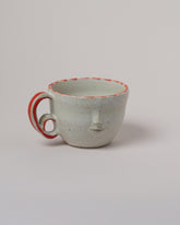 Rami Kim Red Dash Accent Face Mug With Double Loop Handle on light color background.
