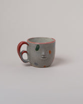Rami Kim Red Dream Face Mug With Double Loop Handle on light color background.