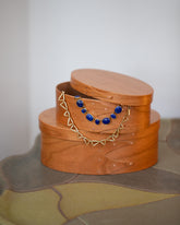Styled image featuring the Rikke Falkow 6" and 7" Cherry Wood Oval Boxes, with the Apparition Necklace and Gold Flexure Necklace.