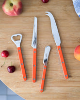 Styled image featuring the Sabre Paris Orange Bottle Opener, Orange Tomato Knife, Orange Butter Spreader & Orange Cheese Knife.