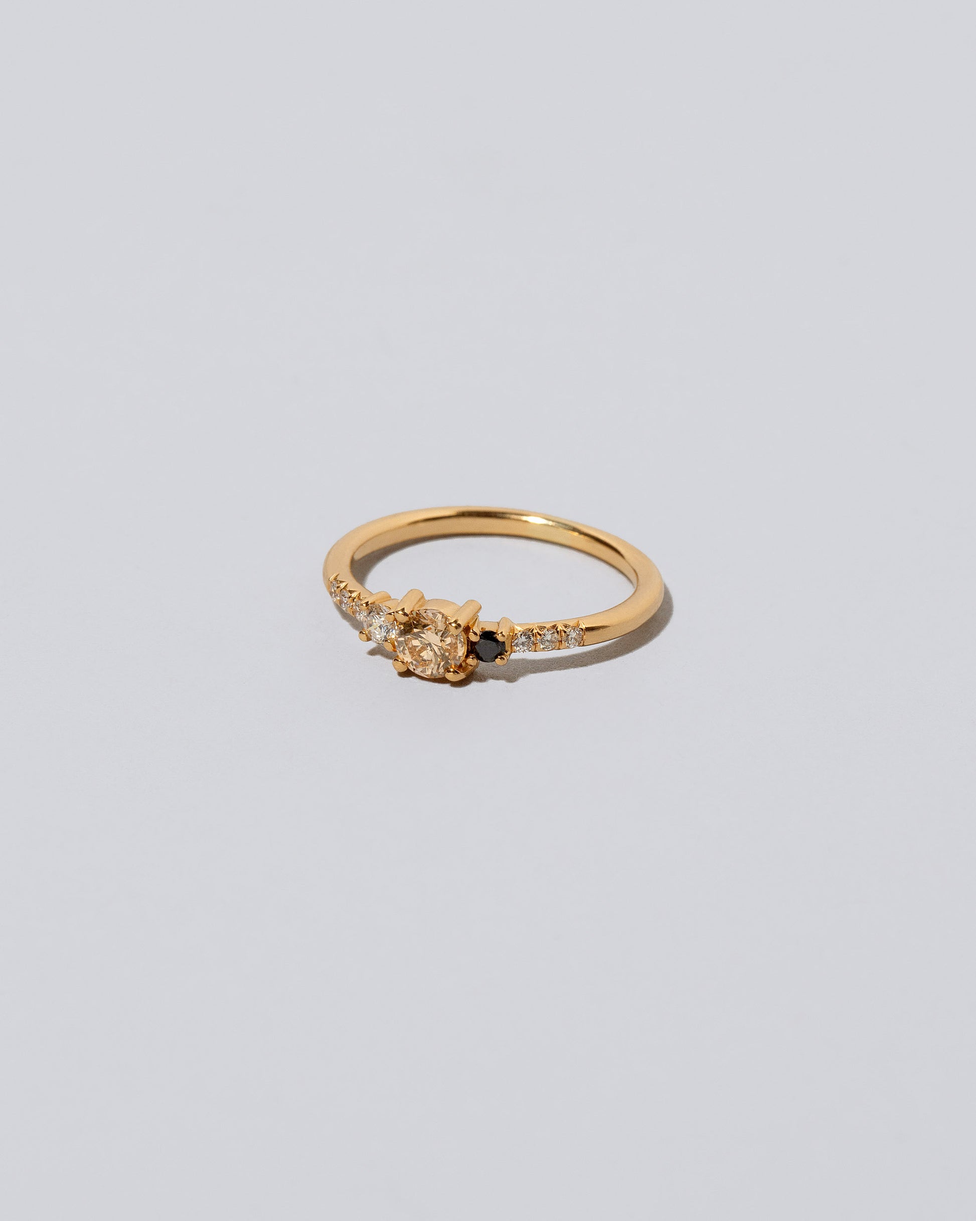 View from the side of the Champagne & Black Diamond Patira Ring on light color background.