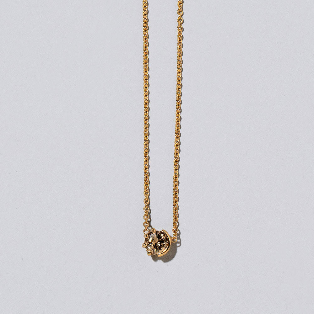 product_details::Closeup view the champagne Diamond Sun & Moon Necklace on light color background.