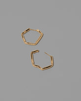 Detail view of the Gold Crimp Hoop Earrings on light color background.