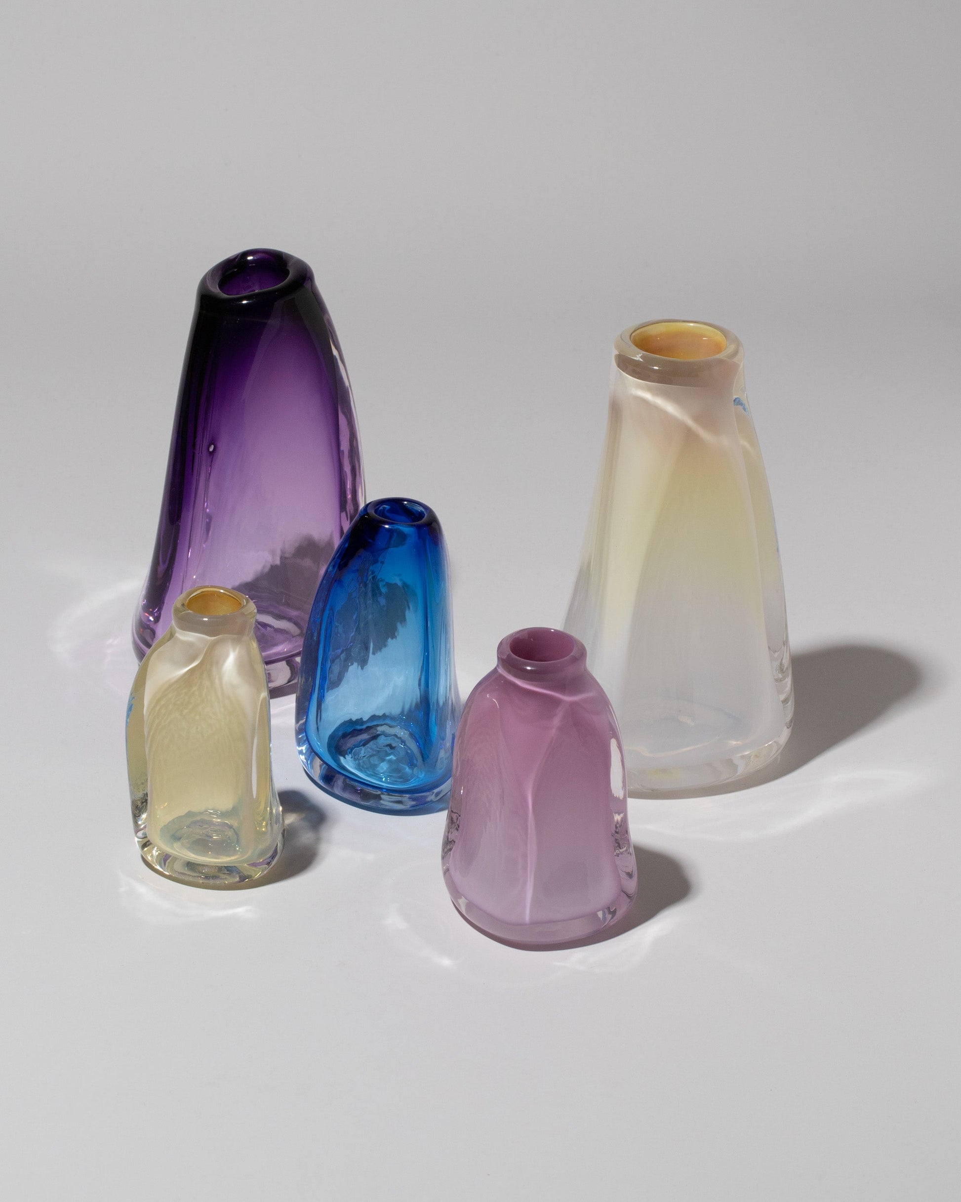 Group of BaleFire Glass Small Lilac, Small Egyptian Blue, Small Vanilla, Large Vanilla and Large Amethyst Suspension Vases on light color background.