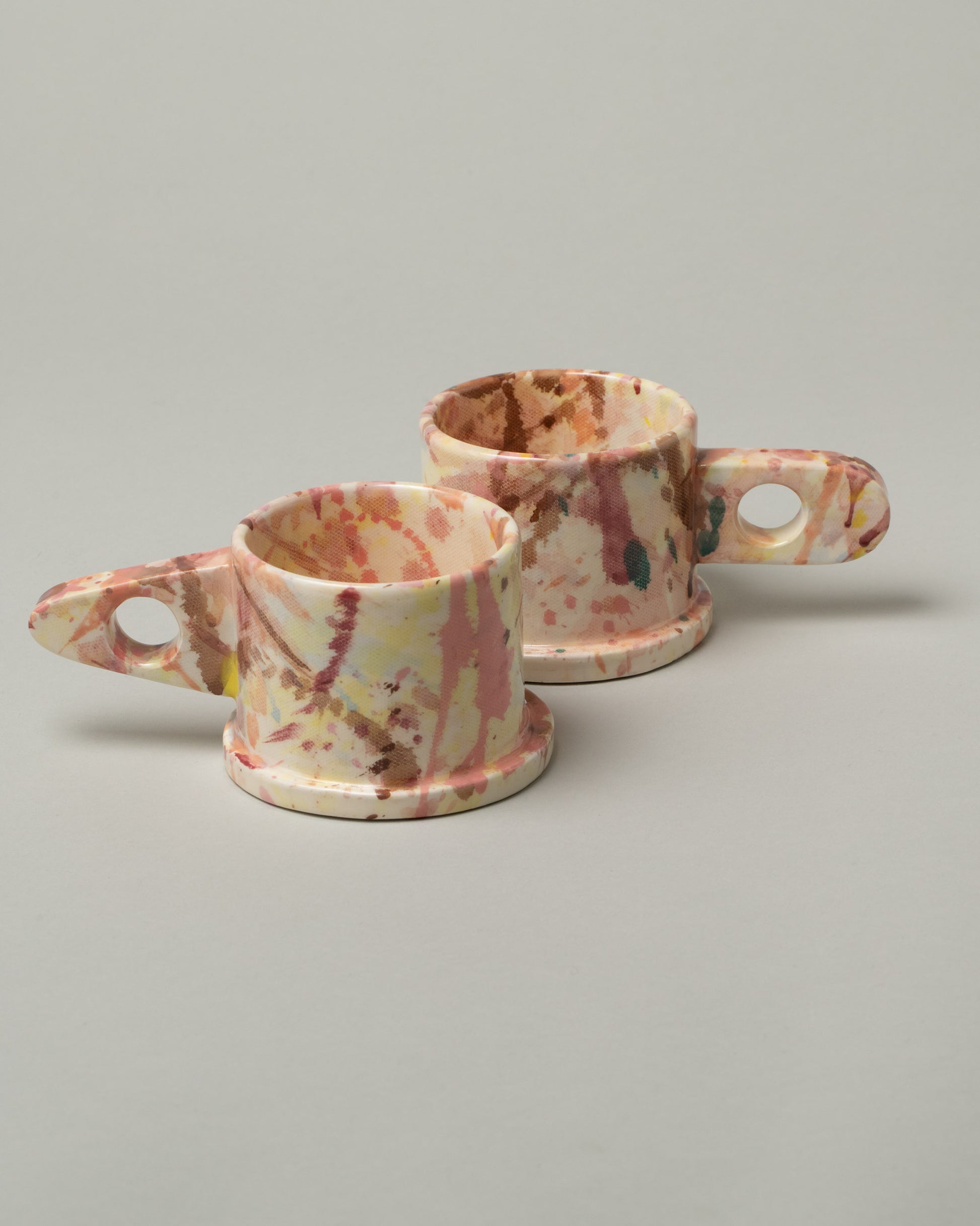 Group of Echo Park Pottery by Peter Shire Triangle Handle Dusty Rose Splatter Mug and Round Handle Dusty Rose Splatter Mug on light color background.