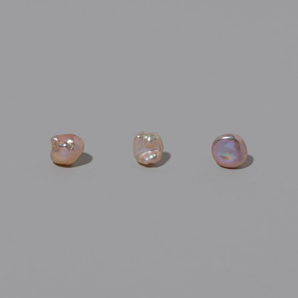 product_details::Closeup details of a group of Blush Lagniappe Pearl Stud Earring Singles on light color background.