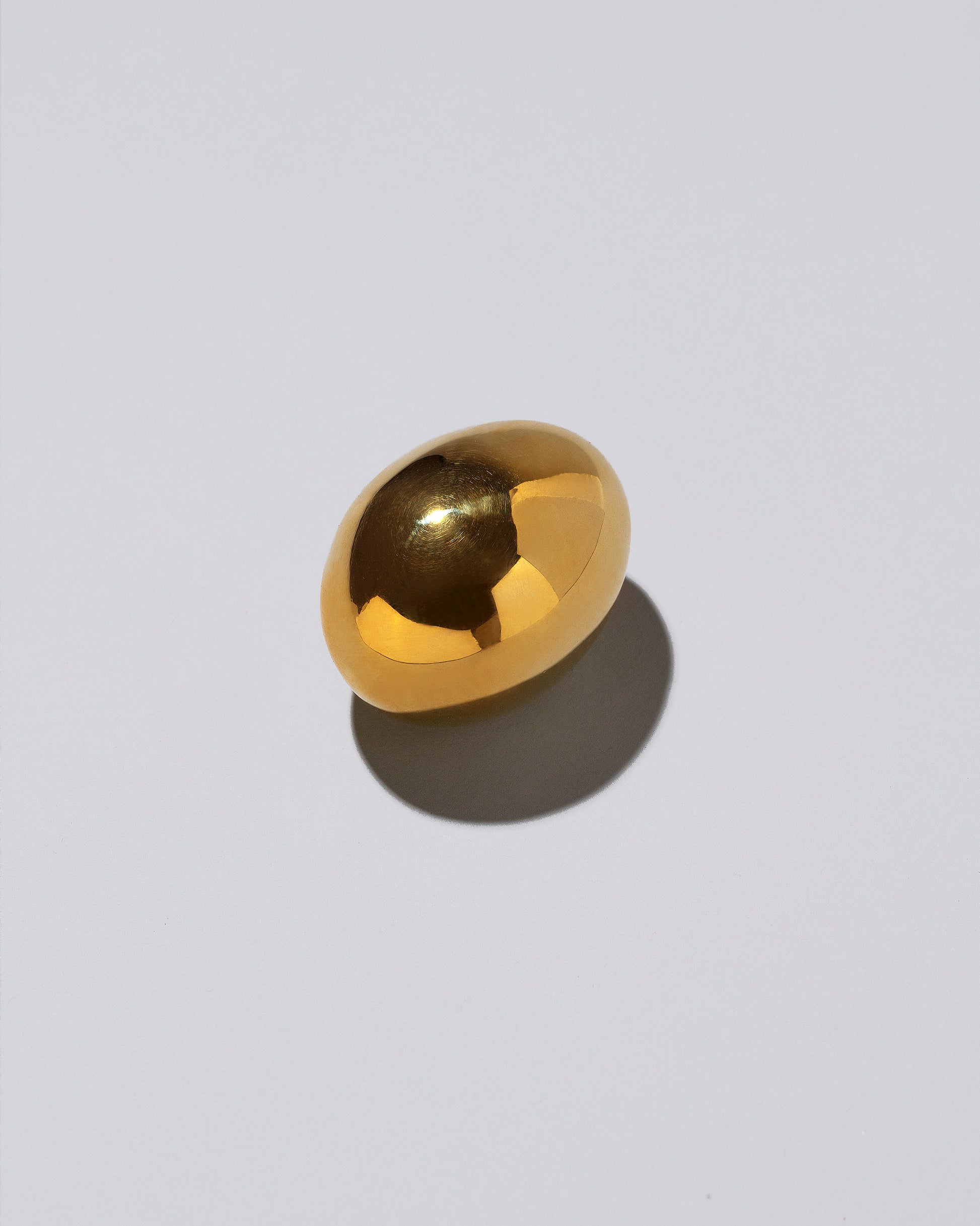 View from the side of the Carl Auböck Brass Egg Paperweight on light color background.