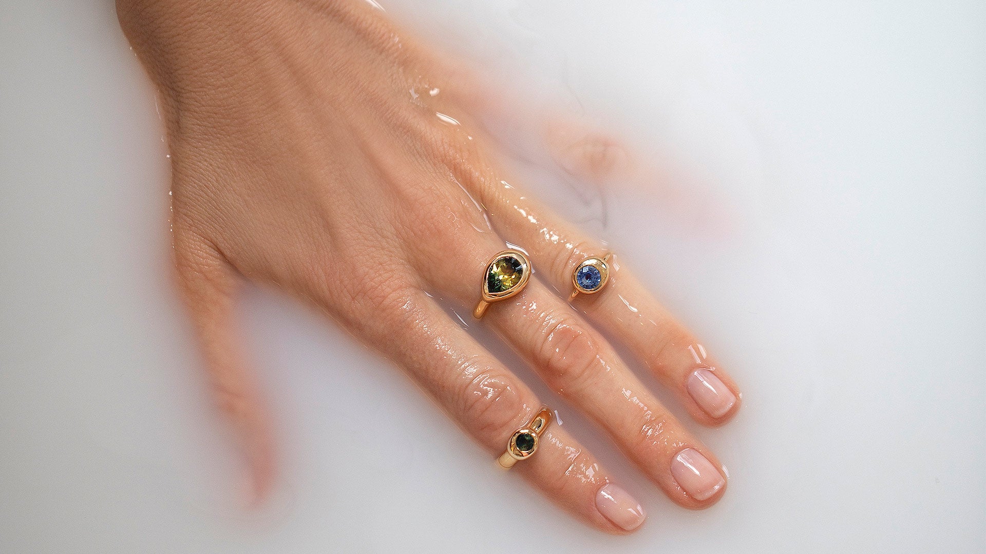 Editorial photo of hand wearing rings from the Level Collection, in milky water.