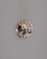 Silje Lindrup White Hands One Orange Glass Wall Clock on light color background.