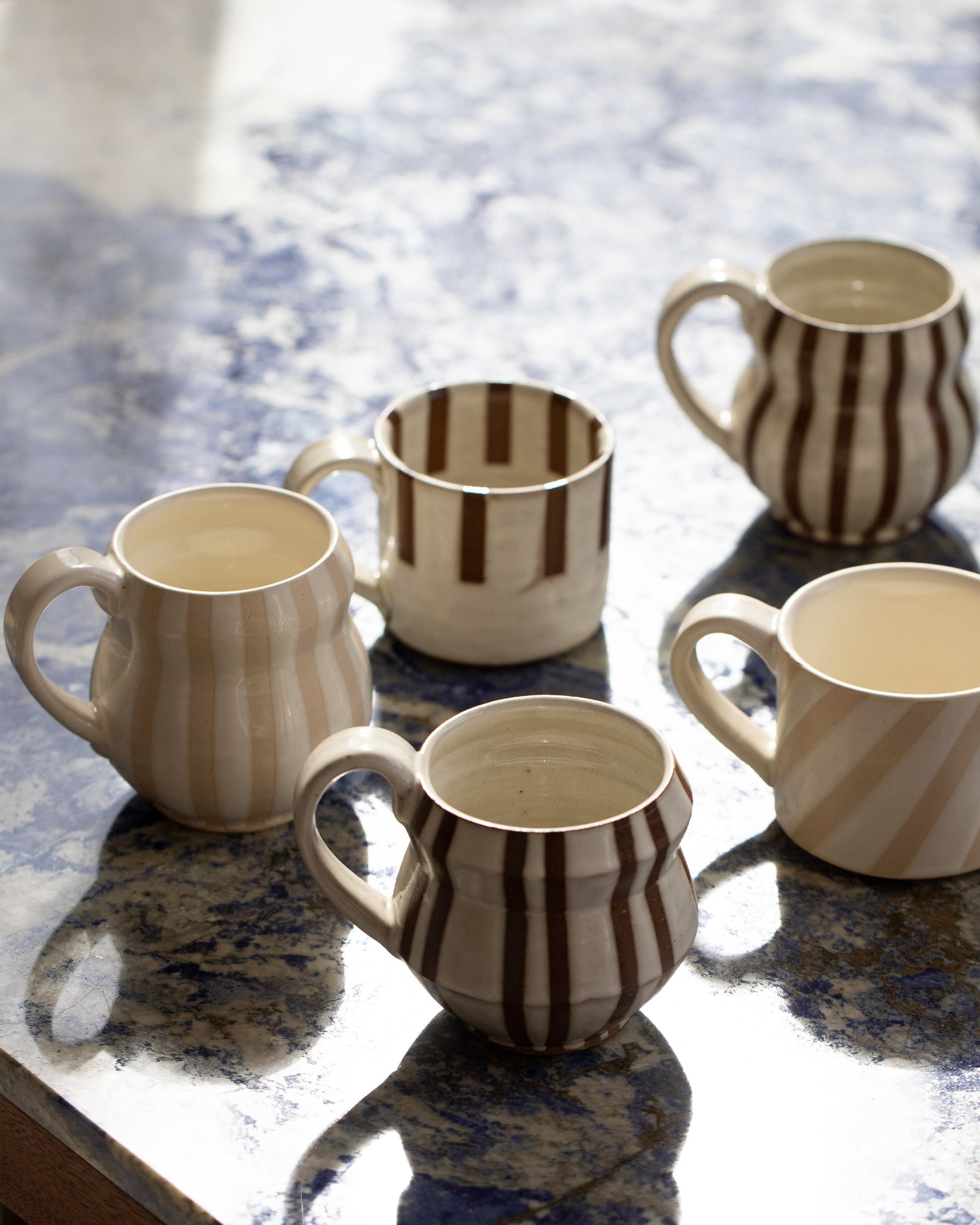 Styled image of Jeremy Ayers Brown and White Bubble Mugs, Half Striped Mug, White Diagonal Stripe Mug and and Brown Angle Mug.