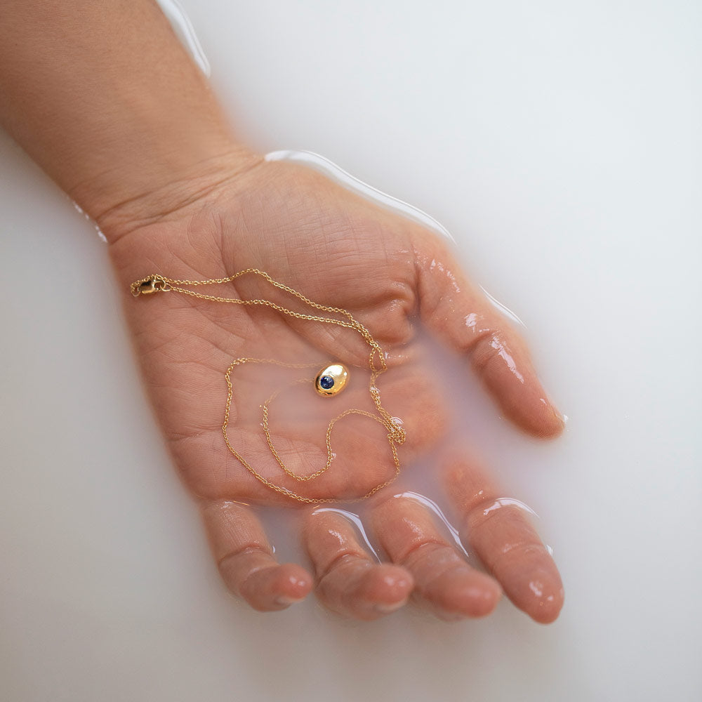 product_details::Gold Bicolor Blue Sapphire Level Necklace in hand.