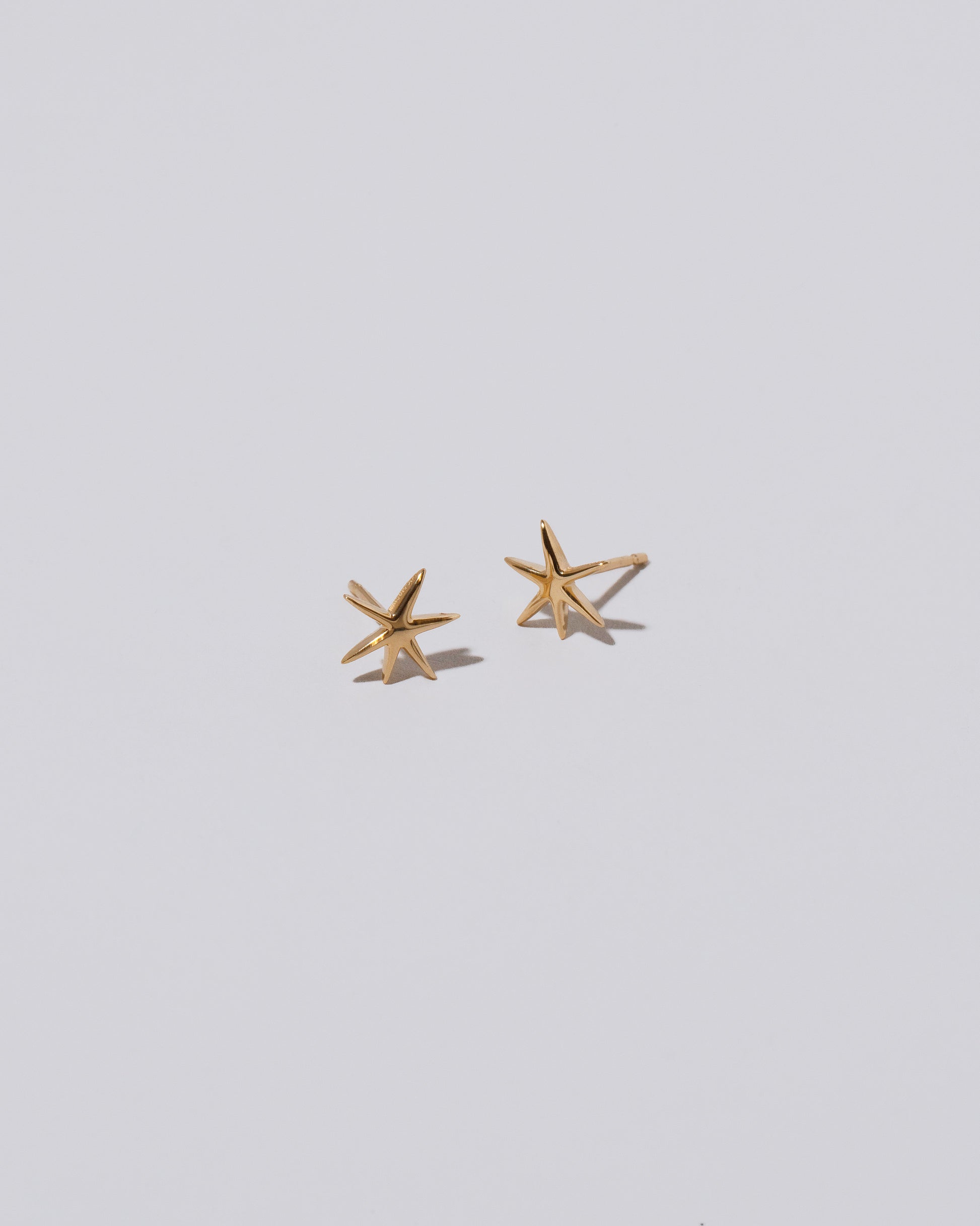 Gold Small Verve Six Point Star Stud Earrings on light color background.'