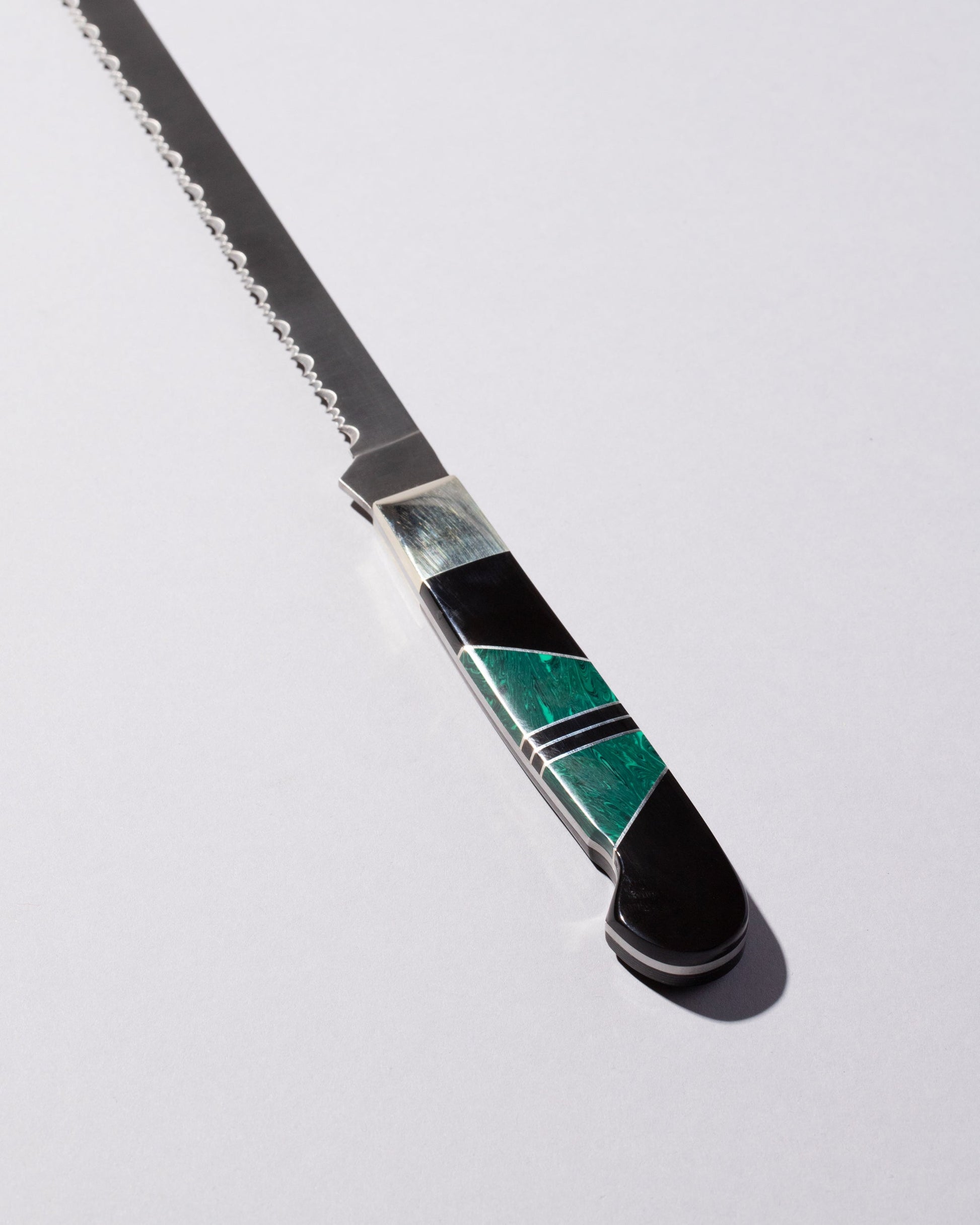 Closeup details of the Santa Fe Stoneworks Jet & Malachite Bread Knife on light color background.