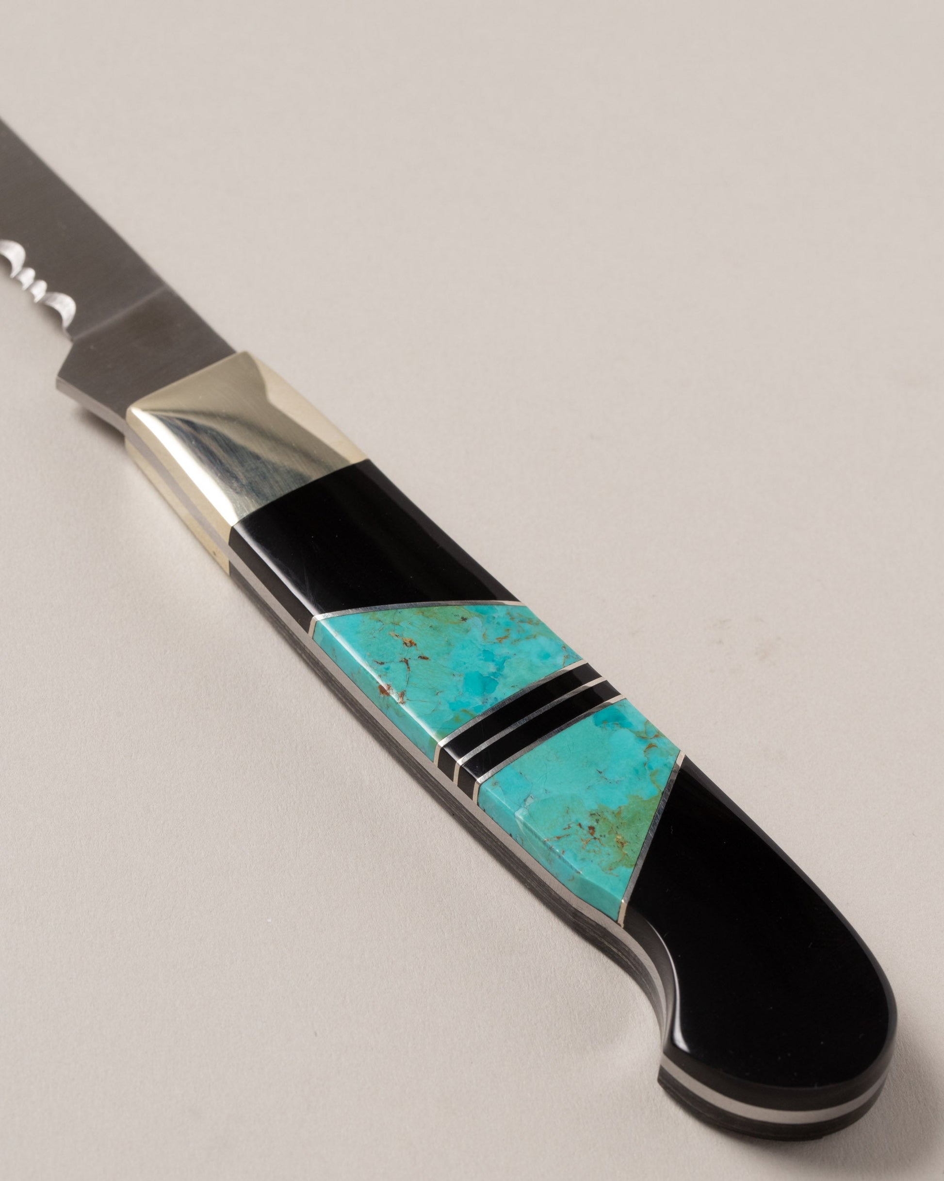 Closeup details of the Santa Fe Stoneworks Jet & Turquoise Bread Knife on light color background.