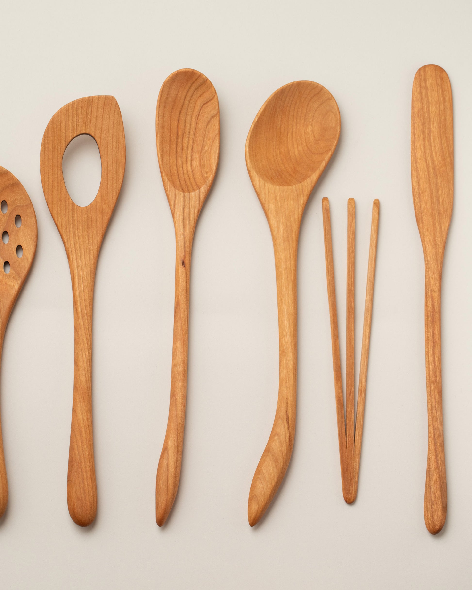 Jonathan's Spoons Skimmer Spoon, Air Spoon, Slim Spoon, Sauté Spoon, Small Wood Whisk and Deli Spreader on light color background.